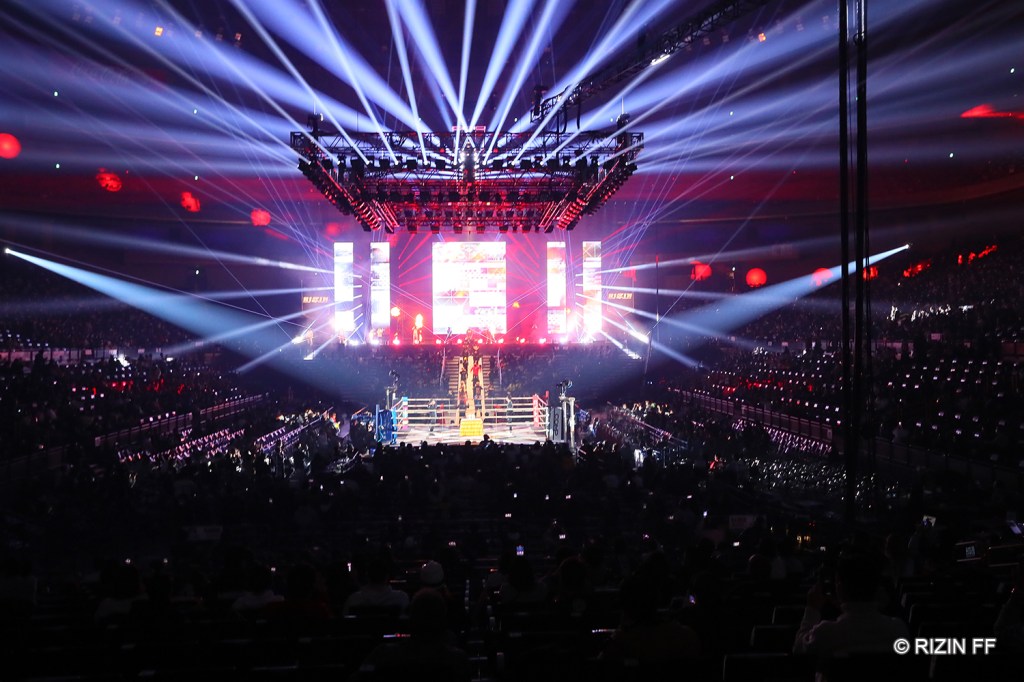 A wide shot of the Saitama Super Arena in Saitama, Japan, which has a lit stage and lights around.