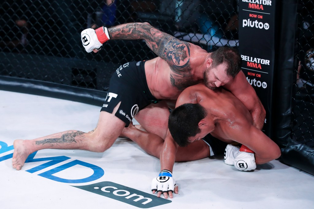 A grounded Ryan Bader throws a right hook to the head of Lyoto Machida, who is being held down on his side.