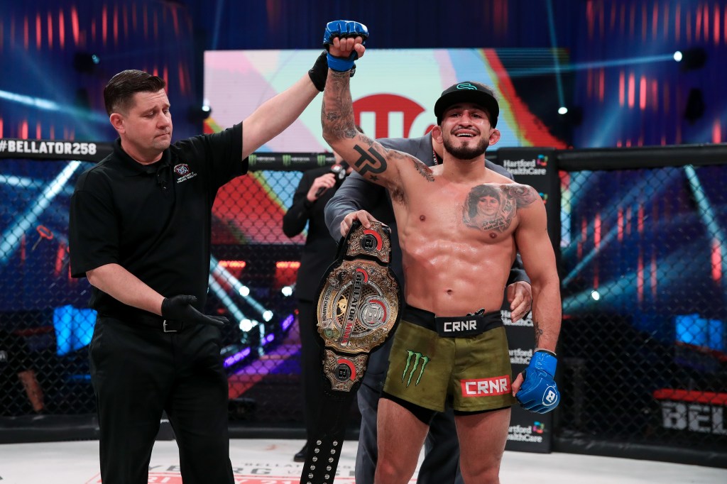 Sergio Pettis gets a Bellator belt wrapped around his waist while a referee raises his right arm.