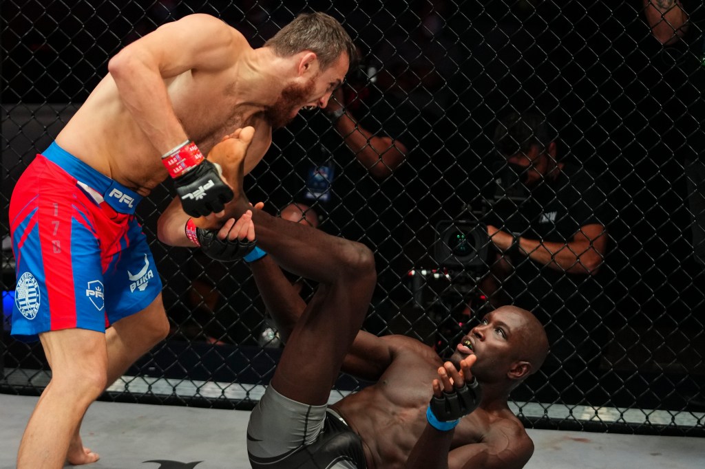 Magomed Magomedkerimov holds the feet of a grounded Sadibou Sy, who has his arms up.