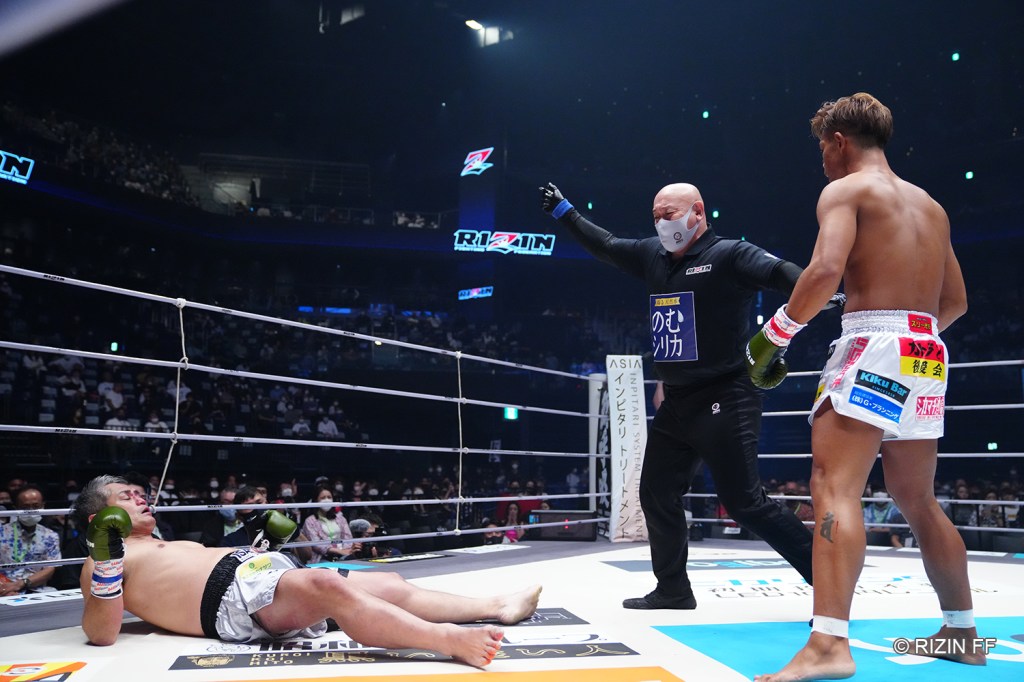 A hurt Lopez Satsuma lays flat on the canvas while a referee backs Hirokatsu Miyagi up.