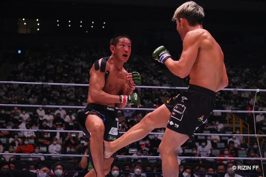 Yoshinori Horie throws a leg kick to Ulka Sasaki, who is wearing athletic tape around his shoulders.