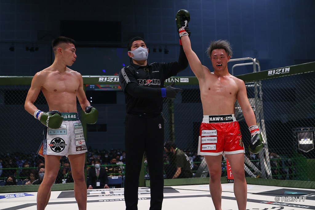 Taiki gets his arm raised by a referee in the RIZIN cage. On the other side of the referee was Kota Nakagawa.
