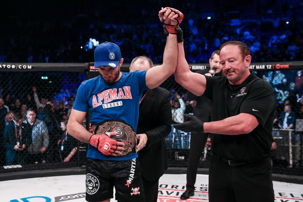 Gegard Mousasi gets his arm raised in the Bellator cage while a belt is placed around his waist.