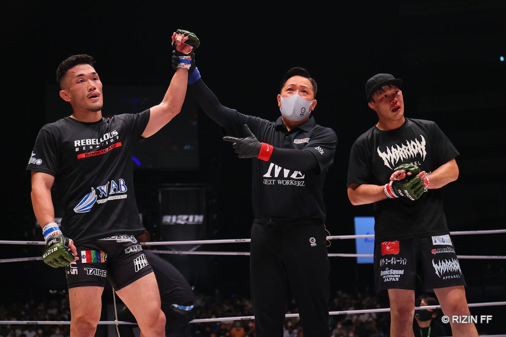 Yoshiki Nakahara gets his arm raised by a referee in the RIZIN cage. On the other side of him, opponent Tetsuya Seki.