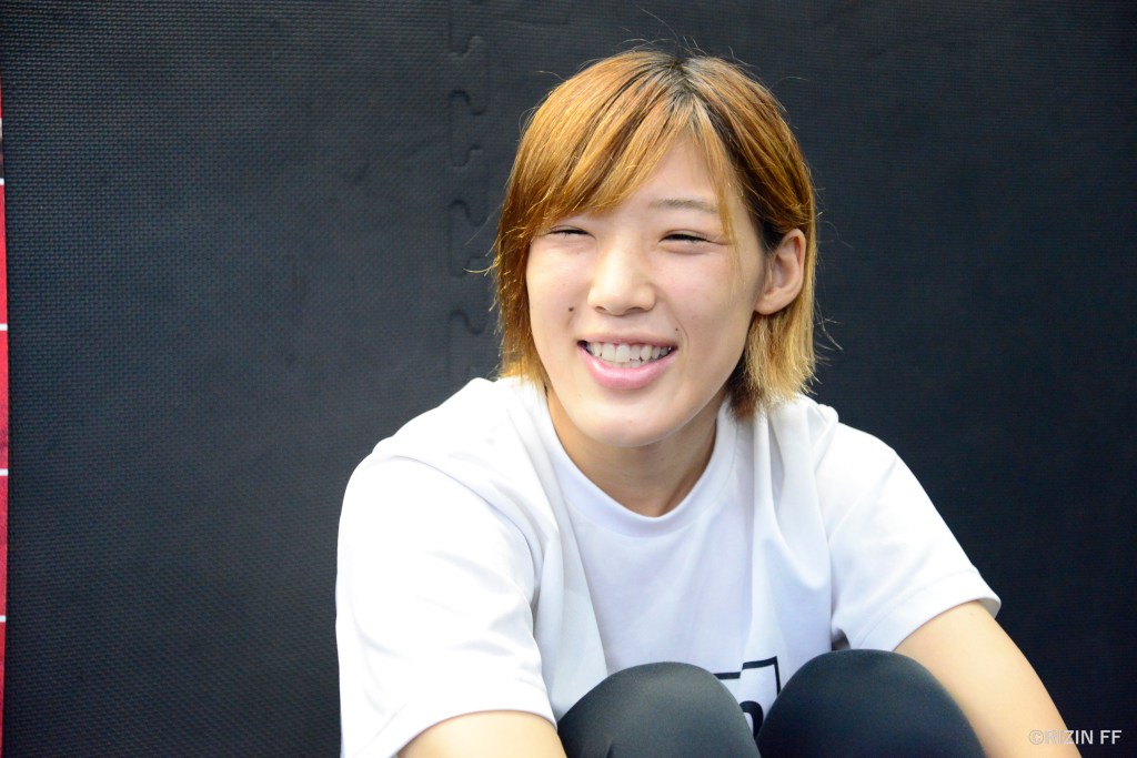 Seika Izawa sits on a padded floor inside an MMA gym.